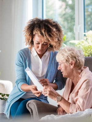 Female home caregiver supporting senior woman in her house, explaining her documents.